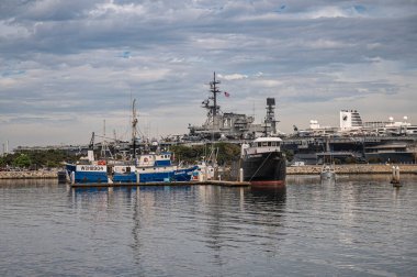 San Diego, California, ABD - 4 Ekim 2021 Embarcadero Tahta Yolu. Tuna Limanı 'na yanaşan balıkçı gemileri Midway uçak gemisi müzesiyle mavi bulutların altında..