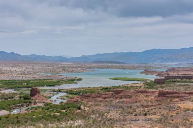 Mead Gölü, Nevada, ABD - 22 Mayıs 2011: Mavi su gölüne doğru ilerleyen Red Rock Butte ve Water Creek ile geniş bir manzara. Yeşil bitki örtüsü ve açık mavi bulut.