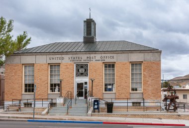 Tonopah, Nevada, ABD - 17 Mayıs 2011: Bulutlu gökyüzünün altında gri çimento süslemeli bej tuğlalı ABD Postane binasının kapatılması. Biraz yeşil yaprak..
