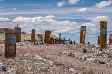 Tonopah, Nevada, ABD - 16 Mayıs 2011: Tarihi Mezarlık. Mavi bulutların altında kayalık, kuru bej çöl zeminine yerleştirilmiş bir grup Redwod tahta stili mezar taşı..