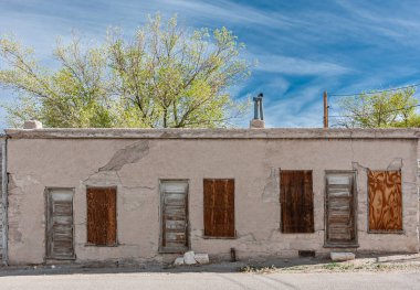 Tonopah, Nevada, ABD - 17 Mayıs 2011: Tarihi Madencilik Parkı. Tahtayla kapatılmış bej harabe bir katlı üç katlı evler. Yukarıdaki yeşil yapraklar ve mavi bulutlar. 