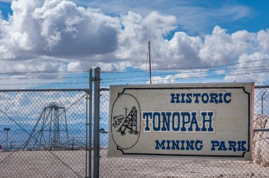 Tonopah, Nevada, ABD - 18 Mayıs 2011: Tarihi Madencilik Parkı. Mavi bulutlar altında çitlere sabitlenmiş açık hava müzesinin isim ve logosuyla imzalayın. Açık kahverengi çöl tabanı.