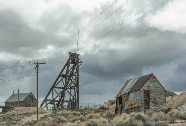 Tonopah Nevada 2011年5月18日 Historical Mining Park 緑の雑草がいくつかあるベージュ茶色の乾燥砂漠の丘の上に隣接する建物と私のシャフトタワー上の大雨灰色の雲の風景 — ストック写真