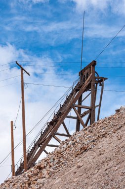 Tonopah, Nevada, ABD - 18 Mayıs 2011: Tarihi Madencilik Parkı. Kahverengi ahşap maden kuyusu asansör kulesi mavi bulutlara karşı, kahverengi-bej şeritlerin ya da atık kaya yığınlarının arkasında.