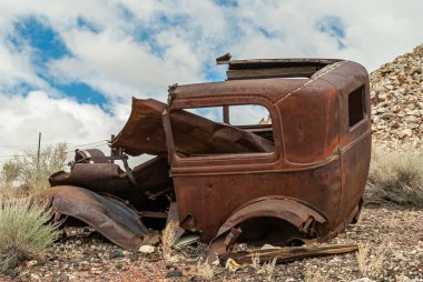 Tonopah, Nevada, ABD - 18 Mayıs 2011: Tarihi Madencilik Parkı. Kahverengi taş tepede mavi bulutların altında bırakılmış paslı klasik arabanın kabuğunun yakın çekimi..