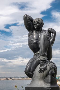 San Diego, California, USA - October 4, 2021: Frontal closeup on black stone Morning statue by Donald Hord on pedestal in front of Wild blue-gray cloudscape, boardwalk in back behind bay water.