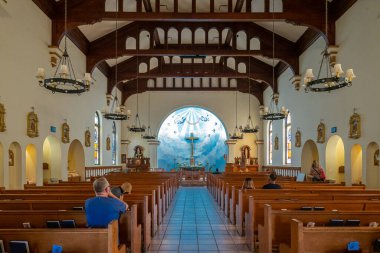 San Diego, California, USA - October 3, 2021: View inside Church of Immaculate Conception looking at altar. Clothing of people on brown wooden benches add color, as does blue reredos.