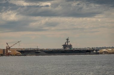 San Diego, California, USA - October 4, 2021: Aircraft Carrier Abraham Lincoln docked at Naval supply center quay under gray cloudscape behind gray bay water.