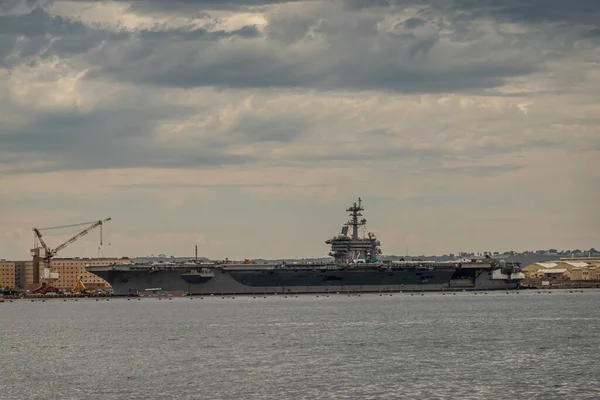 San Diego, California, USA - October 4, 2021: Aircraft Carrier Abraham Lincoln docked at Naval supply center quay under gray cloudscape behind gray bay water.