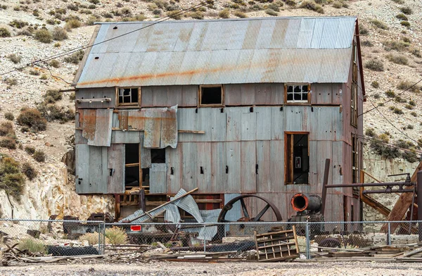 2011年5月19日 アメリカ ネバダ州トノパー 放棄された鉱山の丘に対する乾燥したベージュ砂漠の床に大きな被害を受けた灰色の段ボール金属の背の高い小屋の閉鎖 — ストック写真