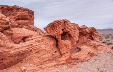Overton, Nevada, ABD - 24 Şubat 2010: Ateş Vadisi. Kuru çöl tabanında çizgiler, çatlaklar ve delikler olan küçük kırmızı kayalar boyunca kalın gri gökyüzünün altında yan çekim..