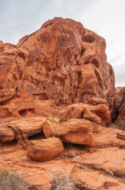 Overton, Nevada, ABD - 25 Şubat 2010: Ateş Vadisi. Kuru çöl zemininde gri gökyüzünün altında gevşek kayaları olan çukurlu kırmızı kaya kayasının yakınına..