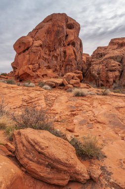 Overton, Nevada, ABD - 25 Şubat 2010: Ateş Vadisi. Kuru çöl zemininin arkasında kayalık duvarlı, mağara benzeri delikleri olan kırmızı kaya kayaları gri bulutların altında..