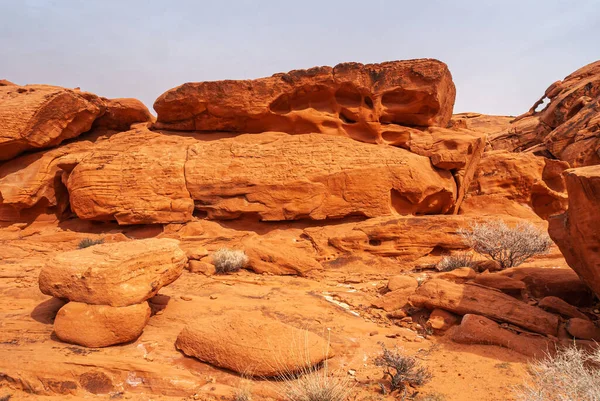 Overton, Nevada, ABD - 25 Şubat 2010: Ateş Vadisi. Düz kırmızı kayalıklı manzara çizgili ve kırık kaya parçaları açık mavi gökyüzünün altında ve önünde kuru çöl tabanı olan..