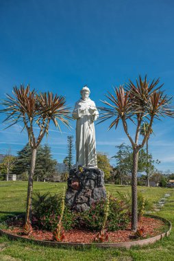 Santa Barbara, Kaliforniya, ABD - 8 Şubat 2022: Calvary Mezarlığı. Kuş, misyoner kurucusu ve botanikçisinin mavi gökyüzünün altındaki beyaz taş heykelinin tepesinde oturur. Yeşil mezar çimenleri ve ağaçlar.