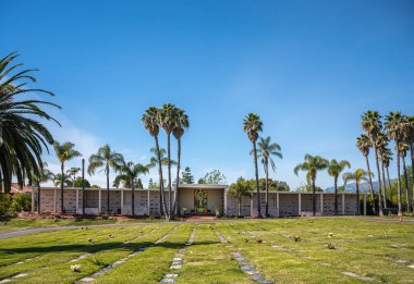 Santa Barbara, Kaliforniya, ABD - 8 Şubat 2022: Calvary Mezarlığı. Büyük bir duvar mezarlığı. Kasa daireleri ve boyalı cam sanat eserleri. Mavi gökyüzünün altında yeşil bir çim ve bolca palmiye ağacı var..