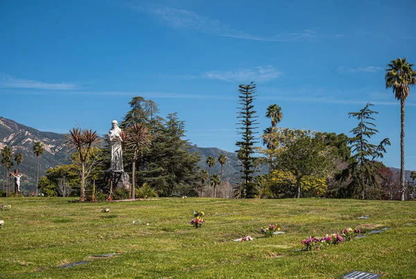 カリフォルニア州サンタバーバラ 2022年2月8日 カルバリー墓地 青空の下で木々の間に白い創設者の宣教師像と緑の埋葬の芝生の風景 前の花 — ストック写真