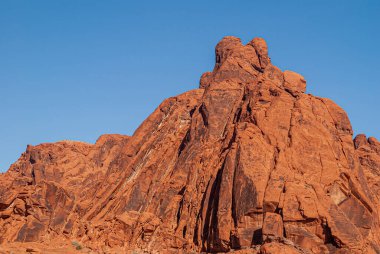 Overton, Nevada, ABD - 11 Aralık 2010: Ateş Vadisi. Kırmızı kaya pelerini dikey çizgiler halinde mavi gökyüzünün altındaki uzun figürün arkasına düşer.. 
