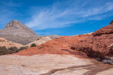 Las Vegas, Nevada, ABD - 23 Şubat 2010 Red Rock Canyon Conservation Area. Kırmızı kaya, bej rengine ve mavi bulutların altındaki ıslak çizgiye hakim. Ufuktaki gri dağ tepesi.
