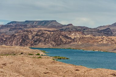 Nelson, Nevada, ABD - 21 Mayıs 2011: Arizona ve Nevada kıyı şeritli Mavi Colorado nehri açık mavi bulutlar altında, her iki tarafında kayalık tepeler olan kuru çöl. Bazı yeşil bitkiler renk ekler.