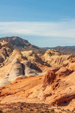 Overton, Nevada, ABD - 24 Şubat 2010: Ateş Vadisi. Açık mavi bulutların altında bej, turuncu ve kırmızı renkli dağların portresi. Önü kuru çöl tabanı..