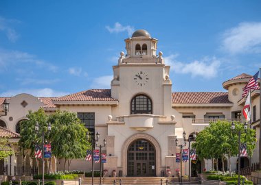 Temecula, CA, USA - April 11, 2022: Old Town neighborhood. Town hall building with clock tower closeup under blue cloudscape. Line of USA flags.