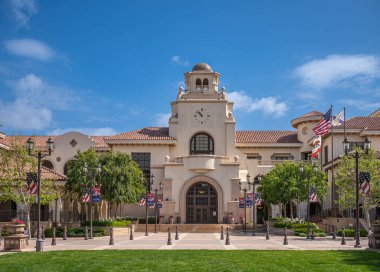 Temecula, CA, USA - April 11, 2022: Old Town neighborhood. Town hall building with clock tower and green lawn up front under blue cloudscape. Line of USA flags to honor fallen heroes.