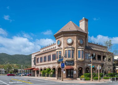 Temecula, CA, USA - April 11, 2022: Old Town neighborhood. Beige stone Bailys restaurant and nightclub on corner under blue cloudscape and mountains in back. Street scenery with cars.