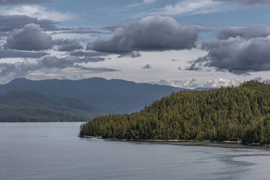 Pasifik Sahil Hattı, Alaska, ABD - 16 Temmuz 2011: Düz mavi Pasifik kıyı şeridi boyunca ağır mavi bulutlu Kanada Rocky Dağları altında güneşli, sık ormanlı tepeler suya ulaşır.