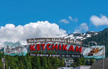 Ketchikan, Alaska, ABD - 17 Temmuz 2011: Dünyanın Somon Başkenti 'ne mavi bulutların altında ve ufukta karla kaplı bir dağın altında duran büyük ücretsiz renkli karşılama tabelası. Yeşil yaprak.