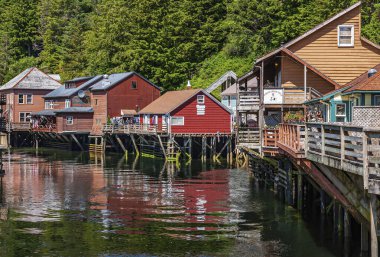 Ketchikan, Alaska, ABD - 17 Temmuz 2011: Poker Creek kuyumcusu ve dere kenarındaki kaleler üzerine inşa edilmiş diğer renkli vintage binalar. Yeşil yeşillik geri geldi. Renkler yansıtıldı.