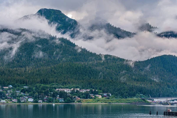 Juneau, Alaska, ABD - 19 Temmuz 2011: Douglas Adası 'ndaki iki yeşil çam ağacı arasında vadide yakalanan gri bulutlar. Gastineau Kanalı kıyısında bir mahalle. Köprü rampasında.. 