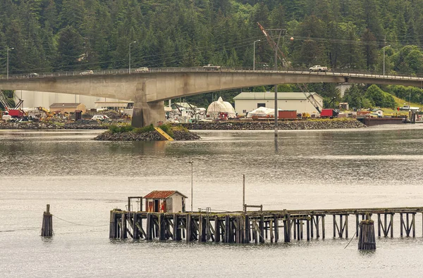 Juneau, Alaska, ABD - 19 Temmuz 2011: Gastineau Kanalı üzerindeki beton köprü üzerinde arabalar ve inşaat alanı arkasında. Önde gri okyanus suyu, arkada yeşil orman. Kulübeli iskele.