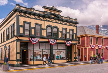 Skagway, Alaska, ABD - 20 Temmuz 2011: 2. Cadde 'deki sarı-yeşil ahşap tren yolu binası. Örtülü bayraklar, posterli pencereler ve de caddedeki insanlar..