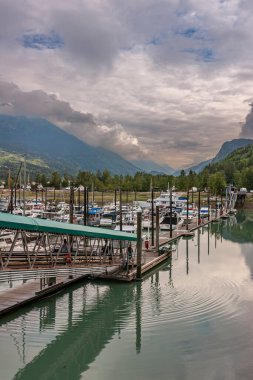 Skagway, Alaska, ABD - 20 Temmuz 2011: Yat limanında önünde yürüyüş yolu olan küçük tekneler. Uzun, karanlık dağ arkadaki bulutlu alana uzanıyor. İkisinin arasında yeşil ormanlık kuşak.