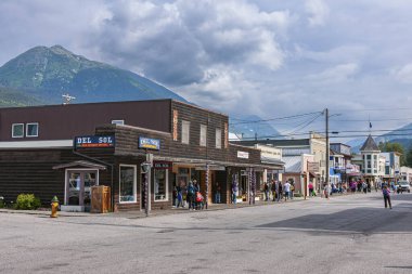Skagway, Alaska, ABD - 20 Temmuz 2011: Del Sol ve Broadway 'deki diğer perakende mağazaları mavi bulutlar ve arkadaki yeşil dağ altında. İnsanlar giyinir ve reklamlar renk katar.