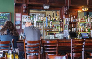 Skagway, Alaska, ABD - 20 Temmuz 2011: Skagway Bira Şirketi 'ndeki kahverengi ahşap barda oturan insanları izleyin. Musluklar, bardaklar ve bir sürü sert içki şişeleri. Etiketler ve posterler renk ekler.