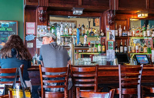 Skagway, Alaska, ABD - 20 Temmuz 2011: Skagway Bira Şirketi 'ndeki kahverengi ahşap barda oturan insanları izleyin. Musluklar, bardaklar ve bir sürü sert içki şişeleri. Etiketler ve posterler renk ekler.