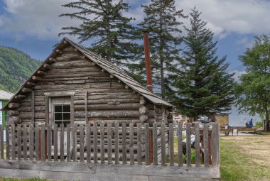 Skagway, Alaska, ABD - 20 Temmuz 2011: Gri ahşap küçük bina mavi bulutların altındaki Tarihi Moore Çiftliği. Dağ yamacında yeşil yapraklar.