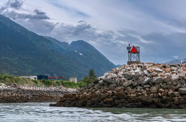 Skagway, Alaska, ABD - 20 Temmuz 2011: Chilkoot körfezinin yukarısındaki Taiya körfezi. Kayalık noktada deniz uyarı işareti. Hamilton İnşaat alanı arkada, mavi bulutların altında. Ufuktaki orman dağı.