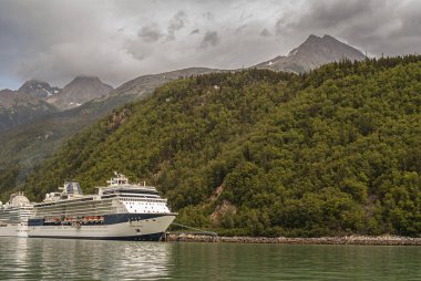 Skagway, Alaska, ABD - 20 Temmuz 2011: Chilkoot körfezinin yukarısındaki Taiya körfezi. Ünlü Millennium yolcu gemisi limanda kapatıldı. Orman, kahverengi bulutların altında yamaçla kaplı..
