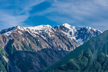 Dischantment Bay, Alaska, ABD - 21 Temmuz 2011: Mavi bulutların altındaki gri dağ sırasının tepesine yakın çekim. Önde yeşil orman kanadı var..