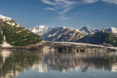 Dischantment Bay, Alaska, ABD - 21 Temmuz 2011: Turner buzulu iniş, ufukta karla kaplı dağlar ve okyanus suyuna yansıyan mavi gökyüzünün altındaki buzdan daha fazla kiri gösteriyor.