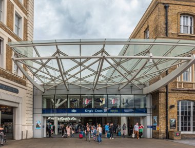 London, Great Britain - July 3, 2022: New side entrance under glass awning of King's Cross railway station. Travellers clothes add color. blue cloudscape and glass awning.