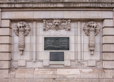 London, Great Britain - July 3, 2022: Beige stone with black information plaque in front of Baker Street subway station features weaponized emblems and lion face, on A501.