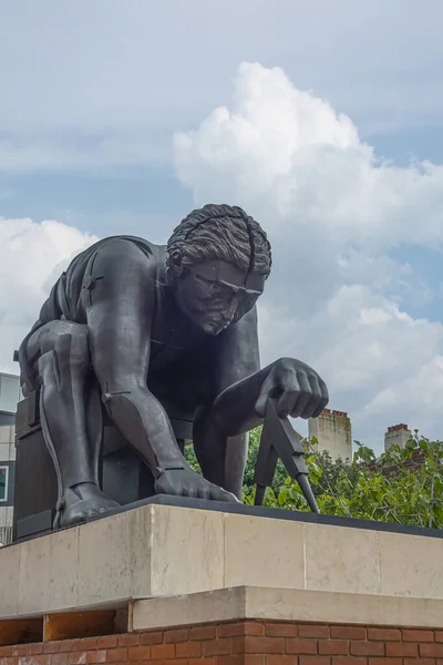 London, Great Britain - July 3, 2022: Closeup of gray Newton Statue on pedestal in front yard of British Library under blue cloudscape. Some green foliage