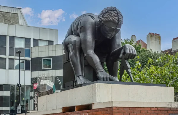 London, Great Britain - July 3, 2022: Closeup of gray Newton Statue on pedestal in front yard of British Library and Theatre under blue cloudscape. Some green foliage