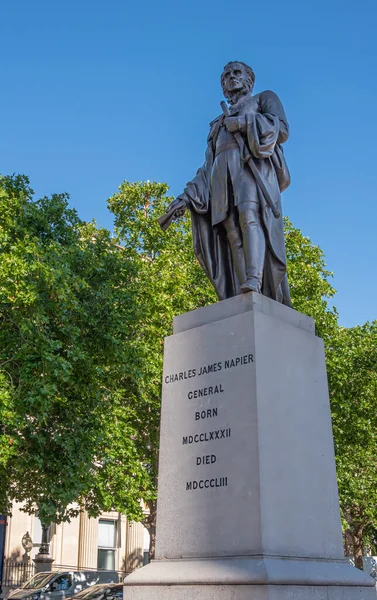 London, UK- July 4, 2022: Trafalgar Square. General Charles James Napier bronze statue on white pedestal under blue sky with green foliage in back.