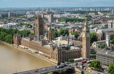 London, UK - July 4, 2022: Seen from London Eye. Scenery with Palace of Westminster, House of Lords, Big Ben, church towers, and urban jungle in back under blue cloudscape. Brown Thames water