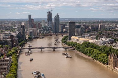 London, UK - July 4, 2022: Seen from London Eye. Lambeth bridge crosses brown water Thames with urban jungle behind. Vauxhall bridge in back under blue cloudscape.
